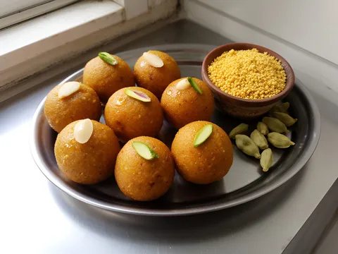 Round golden besan ladoos topped with nut slivers on a steel plate