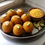 Round golden besan ladoos topped with nut slivers on a steel plate