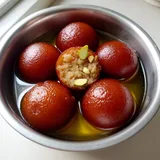 Gulab jamun soaking in sugar syrup, one cut open to show the soft inside
