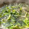Bowl of clear broth with floating vegetables.