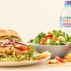Grilled chicken sandwich, salad, apple slices, and water.