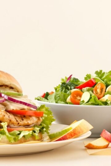 Grilled chicken sandwich, salad, apple slices, and water.