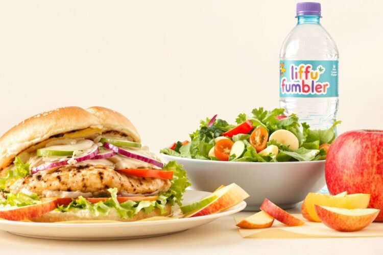 Grilled chicken sandwich, salad, apple slices, and water.