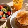 Healthy breakfast spread with fruit, pancakes, and juice.