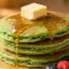 Stack of fluffy green pancakes with syrup and berries.