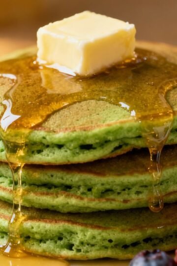 Stack of fluffy green pancakes with syrup and berries.