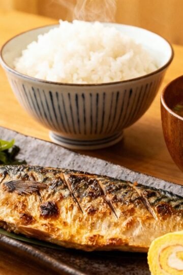 Traditional Japanese breakfast with rice, soup, fish, and pickles.