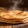 Stack of soft, golden-brown Indian rotis on a wooden surface.