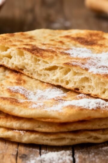 Soft, fluffy rotis stacked on a wooden surface.