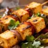 Oven-baked paneer tikka with vegetables on skewers.