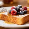 Single serving of French toast with berries and syrup.